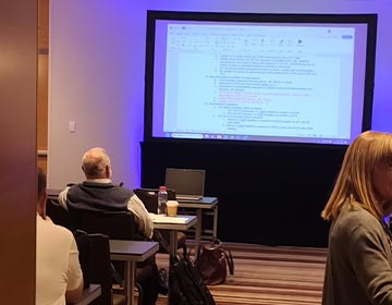 Attendees seated in a conference room watching a projected screen displaying a document during a review session.